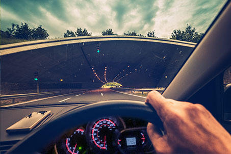 guys hand on his steering wheel driving into a tunnel