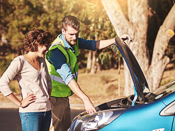 a roadside assistance mechanic fixing a women's car engine